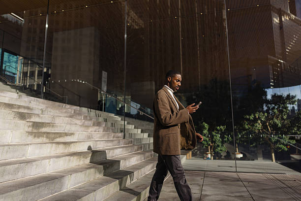 istock Businessman Engaged With Smartphone While Walking Past Modern Glass Architecture 2210800747