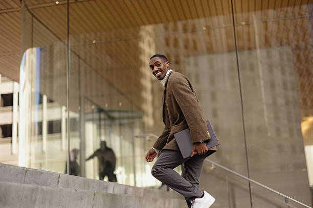 istock Smiling Man Walking into Office Building With a Laptop in Hand 2210800818