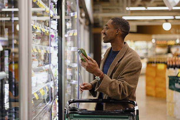 istock Man Shopping in Supermarket While Using Smartphone and Pushing a Cart 2210800884