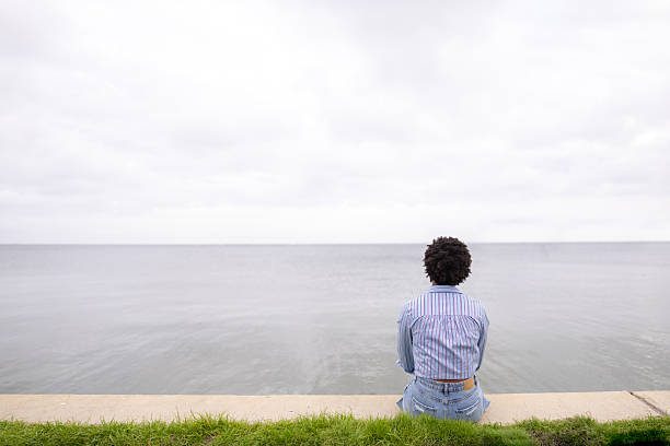 Individual Sitting by a Serene Waterside on an Overcast Day