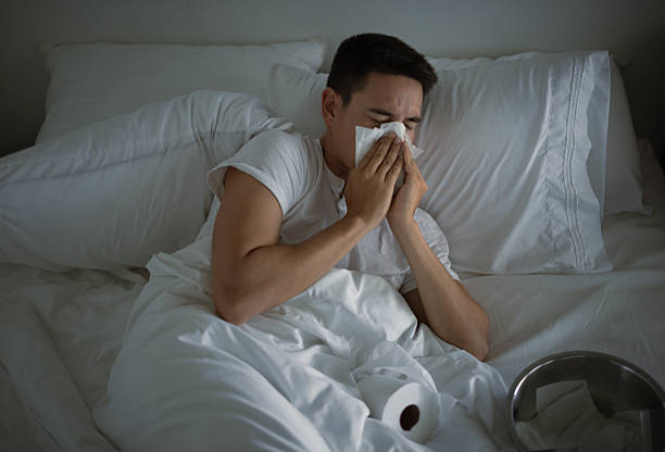 istock Sick man lying in bed blowing his nose. 2210803841