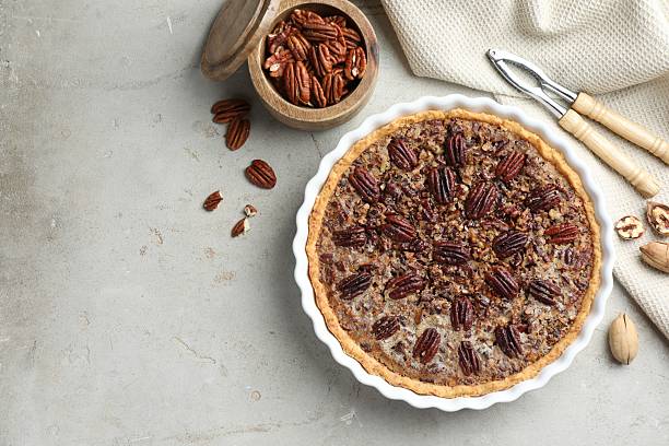 istock Delicious pecan pie in baking dish, nutcracker and fresh nuts on gray textured table, flat lay. Space for text 2210805046