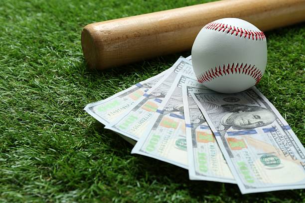 istock Baseball ball, bat and dollar banknotes on green grass outdoors, closeup 2210807273