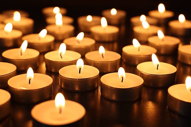 Burning tealight candles on dark surface, closeup