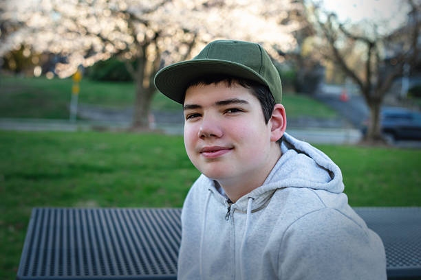 adolescent autiste sur un banc de parc. un garçon de 16 ans avec une casquette verte profite de la soirée de printemps à l’extérieur. - 14 15 ans photos et images de collection