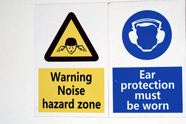 Two labels Warning Noise hazard zone and Ear protection must be worn are attached to white wall on cargo vessel.
