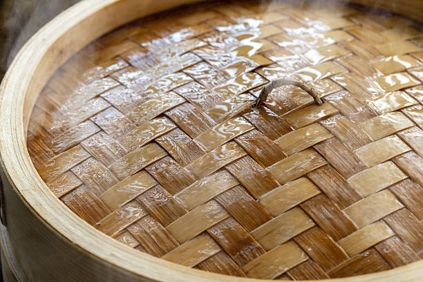 A lid of a bamboo steamer, its surface covered with condensation droplets from steaming, with a slight wisp of steam escaping.