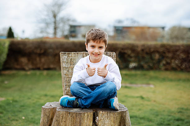 Little child cute boy sitting on a tree stump (looks like a throne) in the forest. Children summer activities
