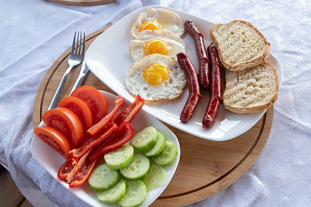 A delicious rustic breakfast arranged on a wooden platter, featuring fried eggs, sausages, fresh vegetables, and toasted bread, captured in a bright and welcoming atmosphere, perfect for highlighting wholesome, countryside living and farm-to-table dining.