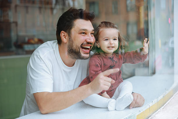 A young father watching outside through the window of a coffee shop with his daughter.