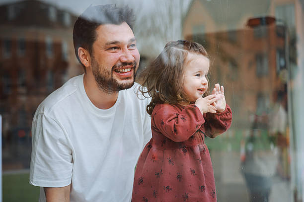 A young father watching outside through the window of a coffee shop with his daughter.