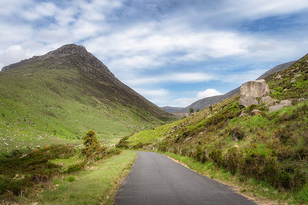 istock A winding mountain road meanders gracefully through lush green hills beneath a dramatic, cloudy sky 2210831089