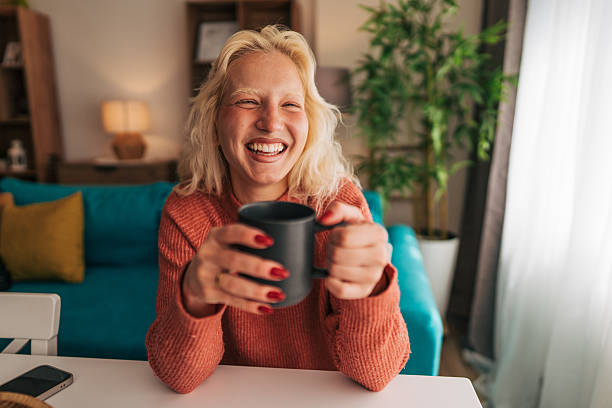 istock Albino woman laughing while drinking coffee at home 2210834136