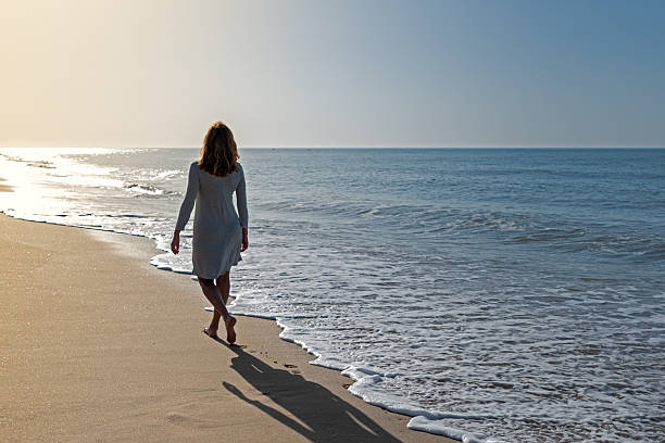 istock Woman walking toward the light along the beach 2210842345