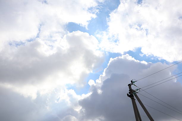 A serene view of fluffy clouds in a bright blue sky with power lines, showcasing natures exquisite beauty