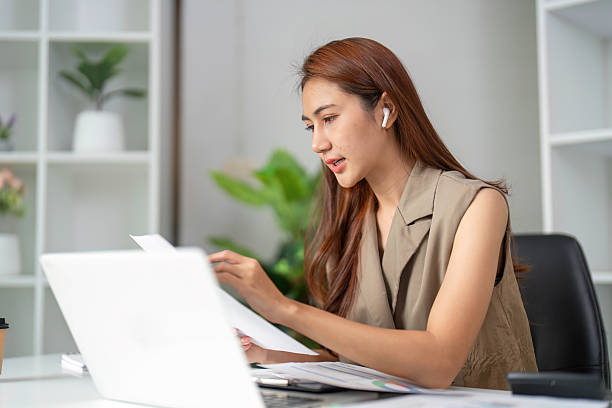 istock Focused Work and Detail Orientation. A woman analyzes documents closely while participating in an online meeting. 2210851121