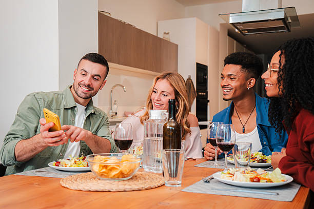 istock Friends enjoying a delightful dinner while sharing laughter and smiles as one shows something interesting on a smartphone during a joyful evening gathering at the dining table together 2210853488
