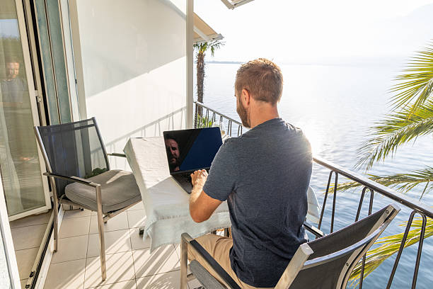 istock Man Working on Laptop at Balcony Overlooking Lake 2210859544