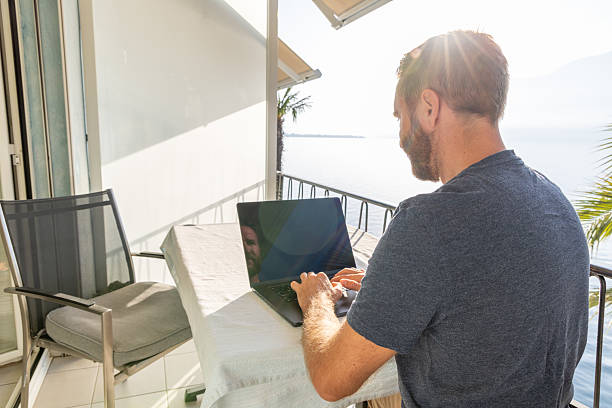 istock Man Working on Laptop at Balcony Overlooking Lake 2210859551