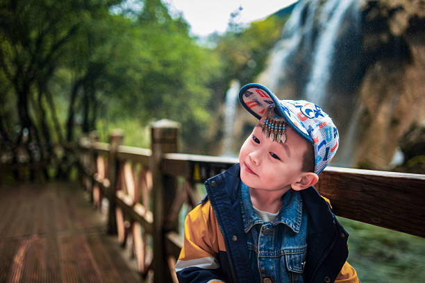 A little boy standing in front of a waterfall with an adorable smile in a stunning natural background