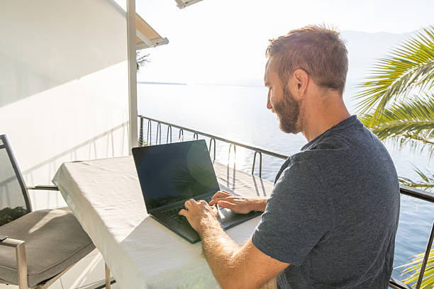 istock Man Working on Laptop at Balcony Overlooking Lake 2210859584