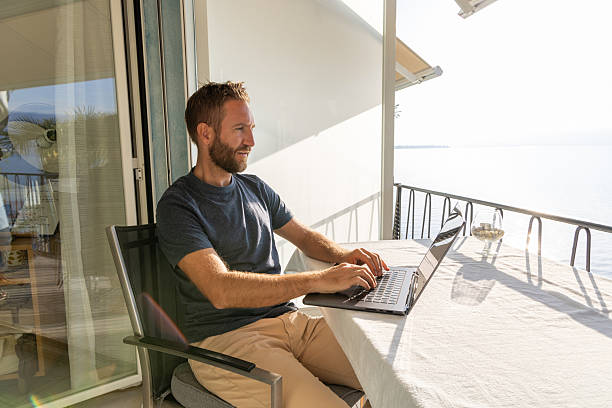 istock Man Working on Laptop at Lakeside Balcony 2210859628