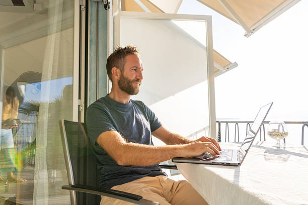 istock Man Working on Laptop at Lakeside Balcony 2210859638