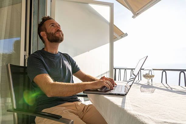 istock Man Working on Laptop at Lakeside Balcony 2210859656