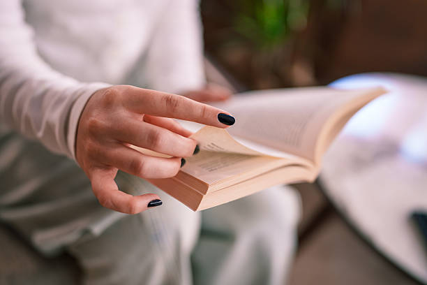 crop image, Hands of woman sitting on sofa with  red wool blanket holding and reading book for relax in night time in living room at home, copy space