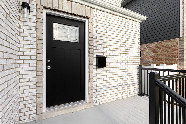 A front door detail on a white brick home with concrete steps and black railing leading to a black front door with a mosaic window.