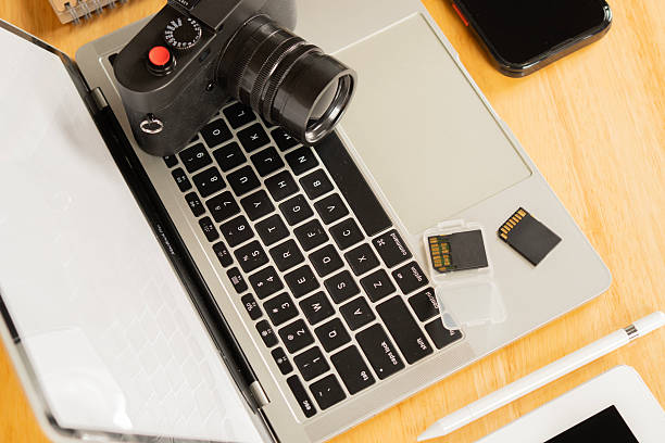 istock Cropped image of a Mobile Phone, a Laptop computer, z pen and notepad with flash Drives and a camera on a wooden table. 2210871962