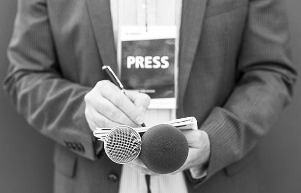 istock Journalist, reporter or correspondent with press pass at media event taking notes on a notepad while holding a microphone. Journalism concept. 2210880300
