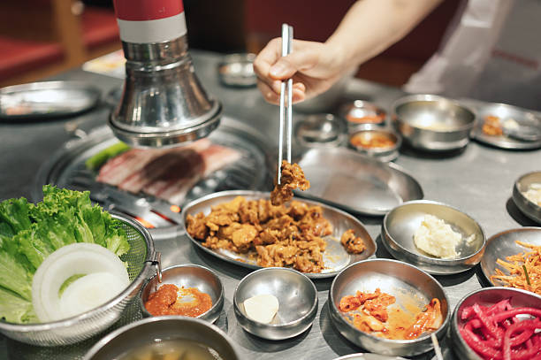 close-up of a korean barbecue table filled with sizzling meat, dipping sauces, and various side dishes. the image represents social dining, authentic korean cuisine, and interactive cooking experiences.