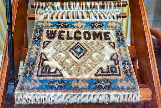 A beautiful welcome mat is being woven on a wooden loom, showcasing intricate patterns and bright colors in a lively artisan market during the day.