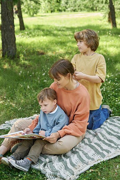istock Mother with Two Boys Reading Book Outdoors 2210899985
