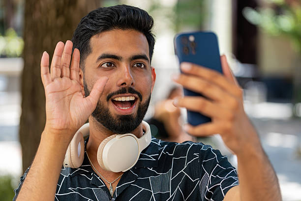 istock Cheerful man tourist smiling friendly at smartphone camera, waving hands gesturing hello hi greeting 2210901701