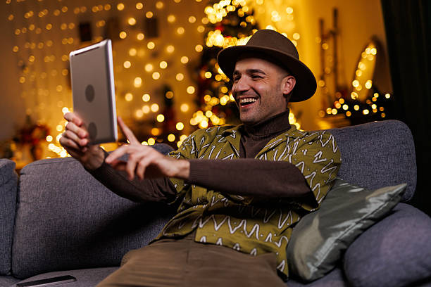 istock Happy man using a tablet while sitting on a couch enjoying a festive ambiance 2210931973