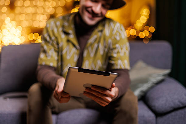 istock Man using a tablet with festive lights in a cozy living room 2210931992