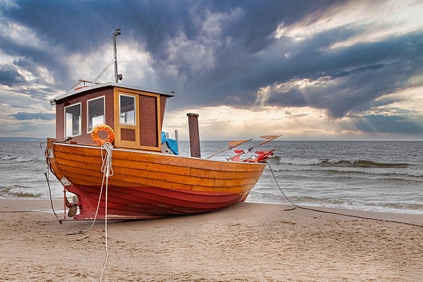 A fishing boat on the beach, in the background a blue cloudy dark sky
