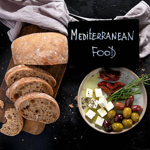 Olive oil and olives in bowls, sliced bread and rosemary on cutting board.