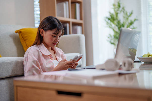istock young woman is working from home while sitting on cozy sofa, focused on her smartphone. bright living space features laptop and plant, creating productive atmosphere.freeelance 2210962301