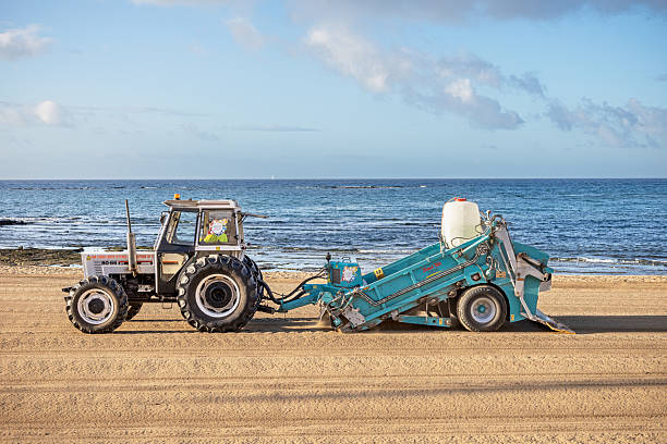 Te Kaha New Zealand - January 31 2022; boats return to shore and being retrieved by red tractor on beach between rocky areas.