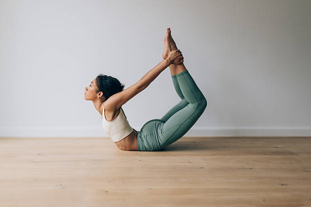 istock Young woman practicing dhanurasana or bow pose on wooden floor 2210964768