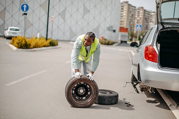 Car after breakdown. Assistance technician changing spare wheel outdoors.