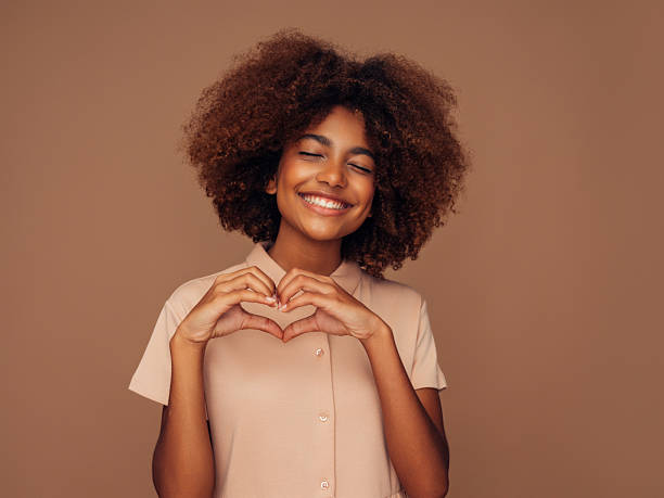 istock Smiling woman forming a heart shape with hands on a neutral background 2210966423