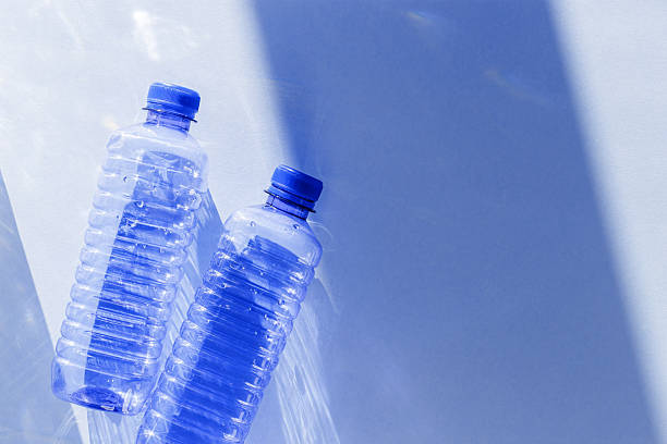istock Blue plastic water bottles on white blue background with sunlight shadow and sun flare, Minimal top view photo, themes of ecology, recycling, sustainable living, reduce disposable plastics 2210966600