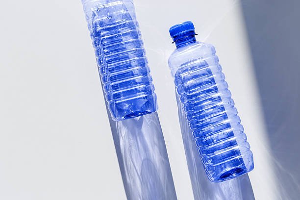 istock Blue plastic water bottles on white blue background with sunlight shadow and sun flare, Minimal top view photo, themes of ecology, recycling, sustainable living, reduce disposable plastics 2210966601