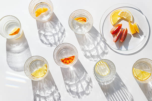 istock Fruit Infused Water in transparent Glasses with Shadows at sunlight on White background. Aesthetic view summer healthy drink with slices of lemon, orange with rainbow sun glare from glass cups, above 2210967734