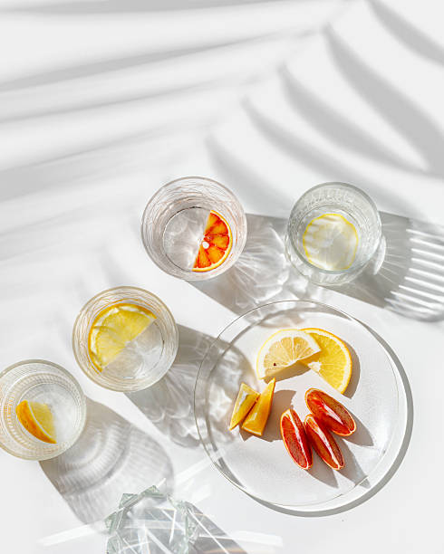 istock Citrus Infused Water in clear Glasses casting artistic light reflections and palm leaf shadows at sunlight. Summer drink concept, minimal pattern, flavored water with yellow red slices of fruit 2210967738