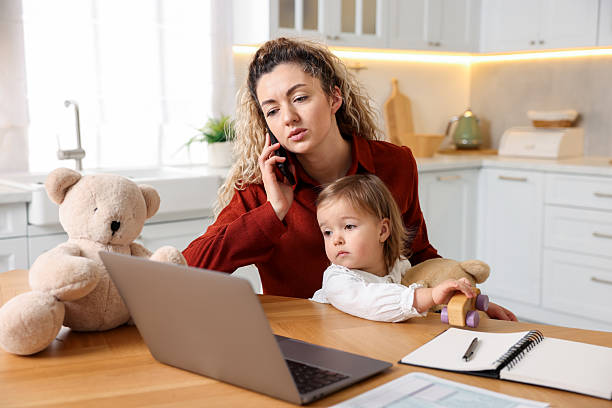 istock Work-family balance. Single mother holding her daughter while talking on smartphone at table in kitchen 2210968841